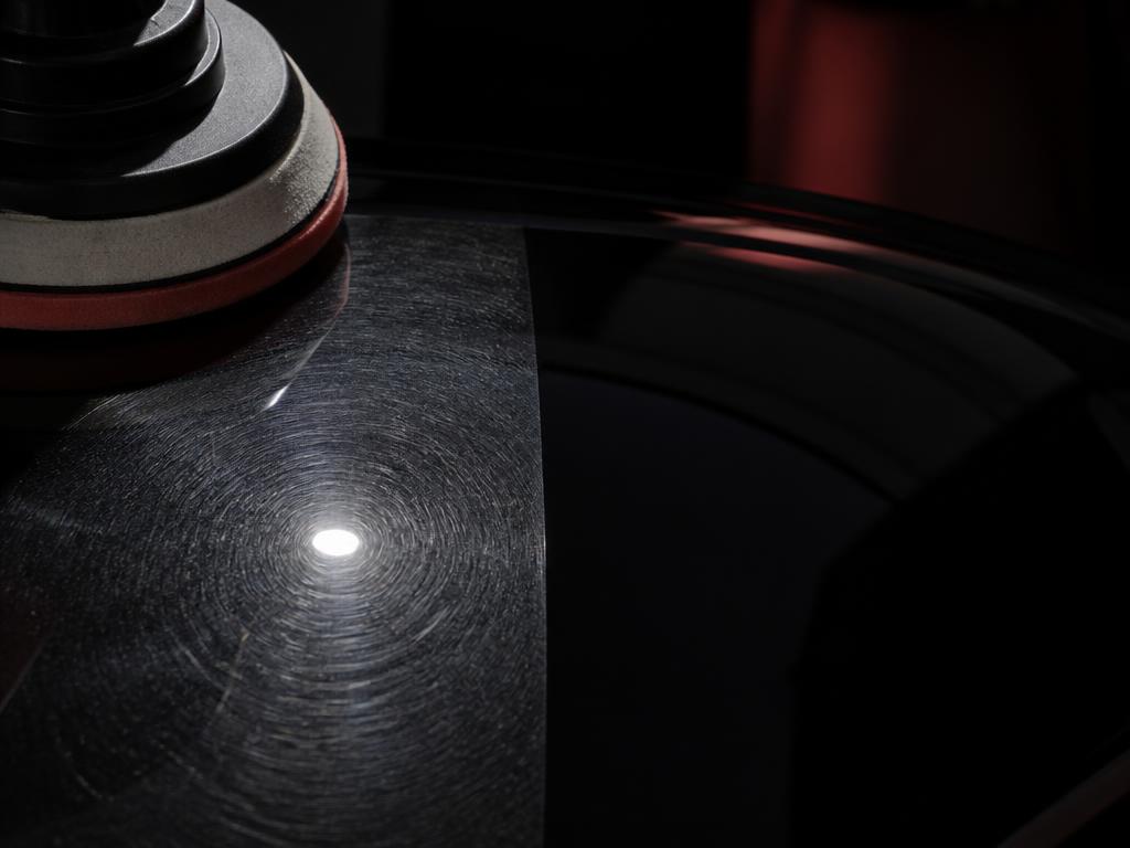 Polishing pad lifting swirl marks from a black car panel under hard raking light